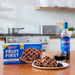 A box of Shop Wyman's Fruit First Waffles - Wild Blueberry and a bottle of Shop Wyman's Wild Blueberry Juice sit on a kitchen counter. A plate showcasing these high-protein breakfast waffles topped with wild blueberries and a glass of juice are ready to enjoy in front.